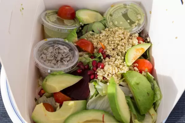 Vegan quinoa salad with avocado, tomato, beetroot, guacamole and seeds in a take-away paperbox