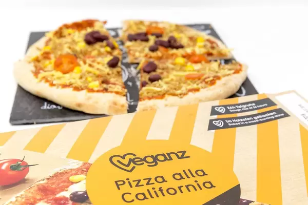 Vegan wood-fired pizza on stone plate in front of pizza carton from Veganz