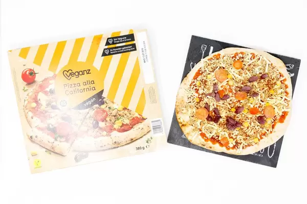 Vegane Backofenpizza auf Pizza-Steinplatte neben Pizzakarton