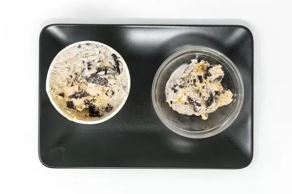 Vegane Ben and Jerrys Eiscreme ohne Milch mit Erdnussbutter und Keks Geschmack in einem Schälchen und Verpackung auf einem schwarzen Teller in der Aufsicht