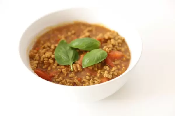 Vegane Bolognese aus Sonnenblumenkernen, zubereitet in Tomatensauce und in einer weißen Schüssel mit Basilikumblättern serviert