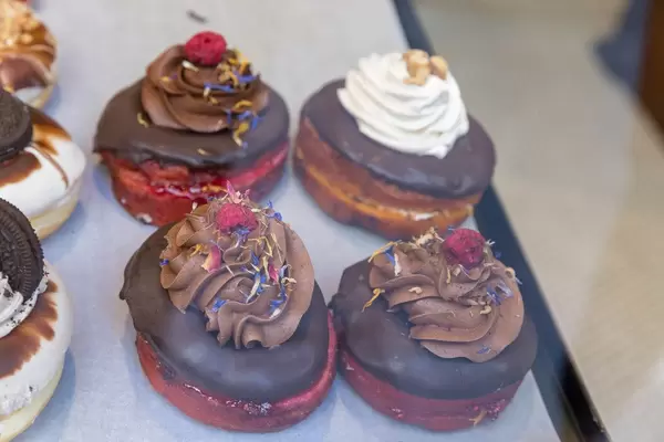 Vegane "Berlina" Donuts mit Schokoladenglasur, Schokosahne, Himbeere und bunten getrockneten Blumenblättern im "chök" in Barcelona, Spanien