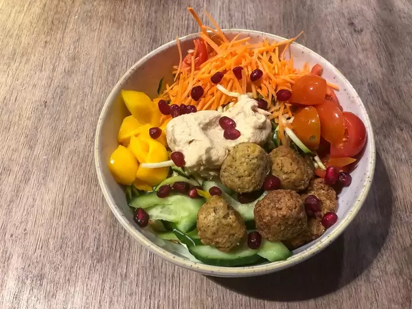 Vegane Schüssel mit Falafel, Hummus, Karotten, Kirschtomaten, Mango, Gurken, Granatapfelkernen: Aufnahme von oben vor hölzernem Hintergrund