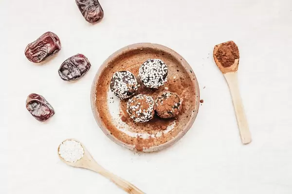 Vegane Sesam Energiebällchen mit Kakaopulver und Datteln auf Tonteller mit Holzlöffeln