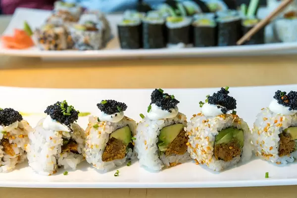 Vegane Sushiplatte "Lucky No Fish" in einer Reihe, mit Kimchi-Sesamkernen verziert und veganem Kaviar-Belag, mit Essstäbchen im Hintergrund