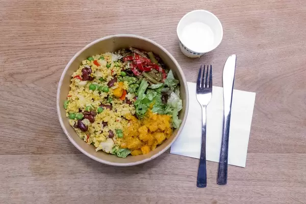 Veganes, asiatisches Mittagessen: Hirsebowle mit Erbsen, Reis, Kidneybohnen, Blumenkohl und Tofu, auf einem Holztisch