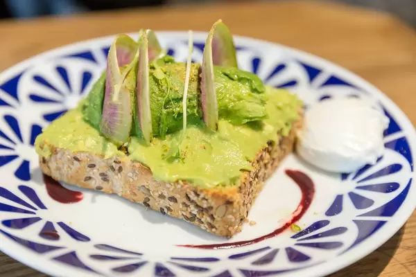 Veganes Avocado Toast aus Vollkorn-Brot mit Guacamole, pochiertem Ei und Acai Soße im Flax&Kale Restaurant in Katalonien