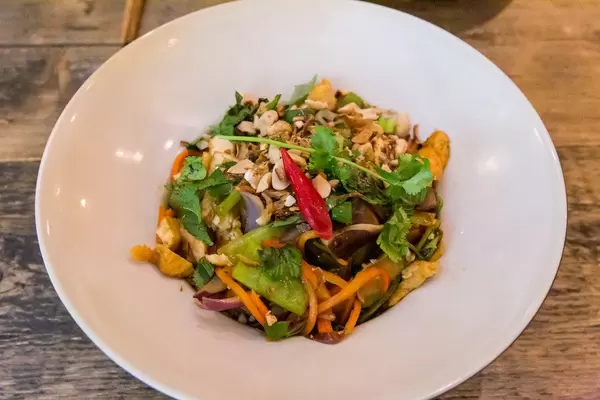 Veganes Bio-Tofu in dünnen Scheiben gebraten mit Zwiebeln, Pak-Choi, Champignons, Zuckererbsen, Bandnudeln und Erdnüssen mit Limetten-Chili Sauce