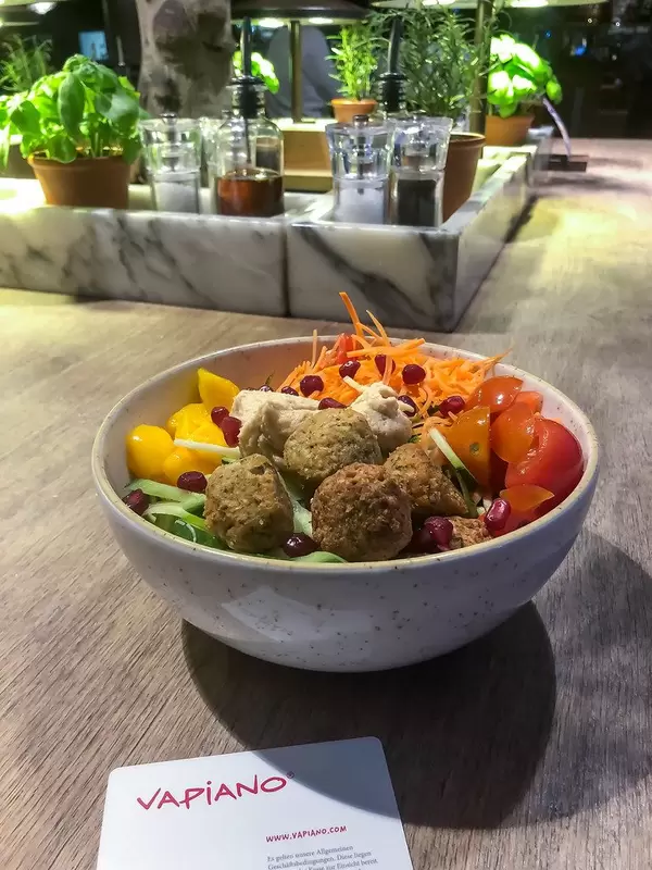 Veganes Essen beim italienischen Restaurant Vapiano mit Falafel, Hummus, Salat, Gemüse und Mango in einer weißen Schüssel