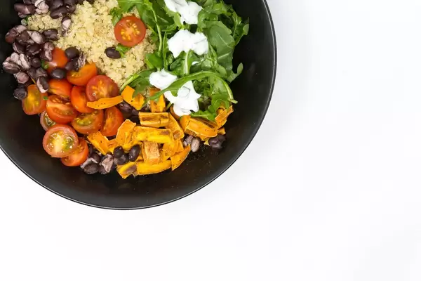 Veganes Essen in schwarzem Teller auf weißem Hintergrund Hello Fresh Kubanische Quinoa Bowl - mit Rucola mit Sauerrahm, schwarzen Bohnen, Kirschtomaten und zimtigen Süßkartoffeln