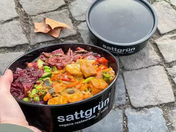 Veganes Essen zum Mitnehmen: schwarze runde Dosen vom veganen Restaurant Sattgrün in Köln