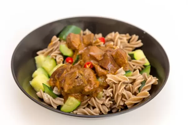 Veganes Gericht im Nahaufnahme: Pasta mit Jackfruit, Gurkeln und rotes Paprika im Currysauce auf schwarzem Teller