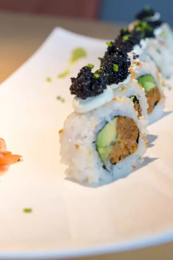Veganes Sushi, aufgereiht auf einem weißen Teller, mit veganem Kaviar verziert, Avocadostückchen, Lauchzwiebel und veganem Thunfisch