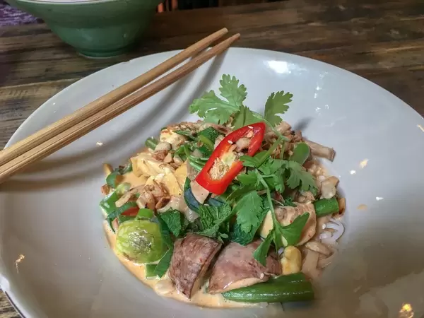 Veganes Tofu-Pilz Gericht im Sauce mit grünes Topping und Paprika mit Eßstäbchen am Rande des Tellers