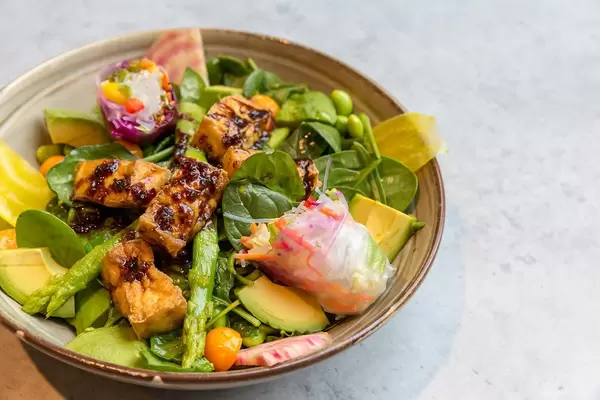 Veganisches Tofu-Gericht mit Spinat, Spargel, Avocado, Minze und Sommerrollen in brauner Schale im Nahaufnahme