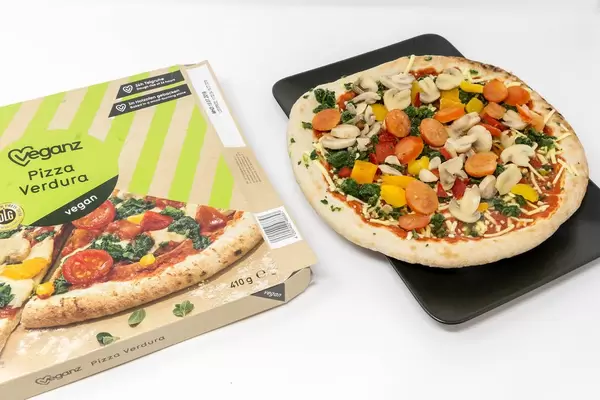 Veganz Pizza Verdura - deep frozen pizza with mushrooms, spinach, paprika and tomatoes and packaging  on a black plate and white background