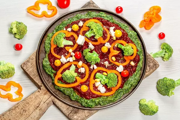 Vegetable pizza with tomatoes, pepper, broccoli and feta cheese with ingredients on the table