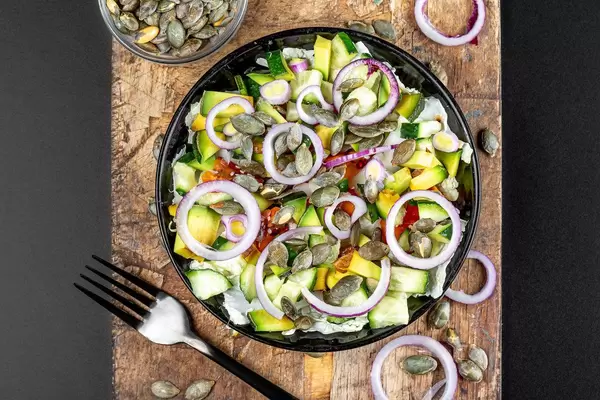 Vegetable salad with pumpkin seeds on an old kitchen board. Top view