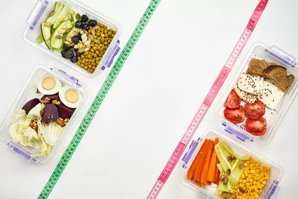 Vegetable salads in food containers and measuring tapes on white background