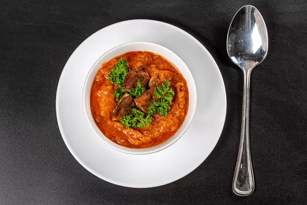 Vegetable soup with carrots, zucchini, chicken fillet and green parsley on a black background, top view