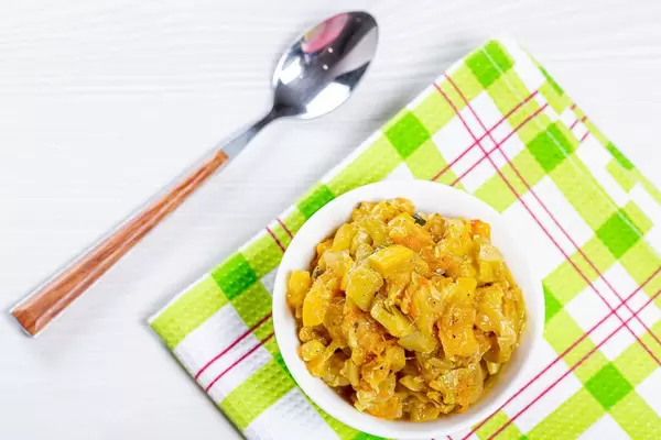 Vegetable stew in white bowl and spoon on table with green dish towel