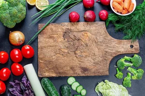 Vegetables and greens frame on a black background and old kitchen Board in the middle