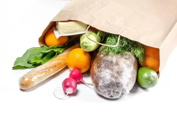 Vegetables, fruits, greens, bread and cheese in a paper bag on a white background. Food shopping concept