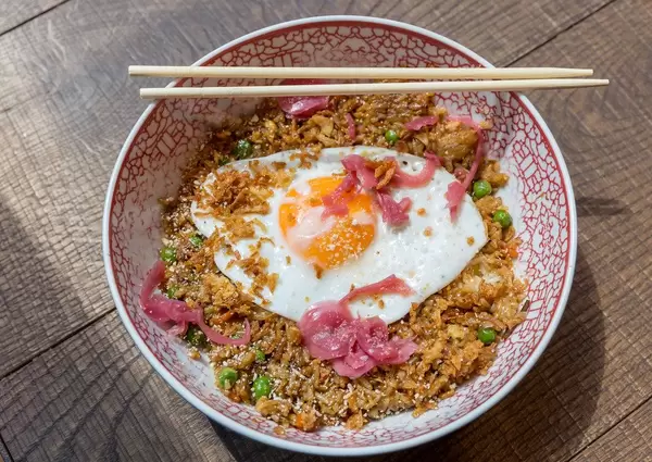 Vegetarian meal in white-red plate with chopsticks: fried rice with onions, carrots, peas, ginger and fried egg