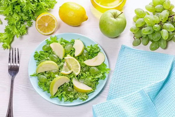 Vegetarian salad with lettuce, fresh Apple slices and grapes on the table with ingredients. Top view (Flip 2019)