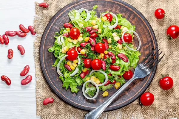 Vegetarian salad with vegetables and red beans in a brown plate on a burlap top View