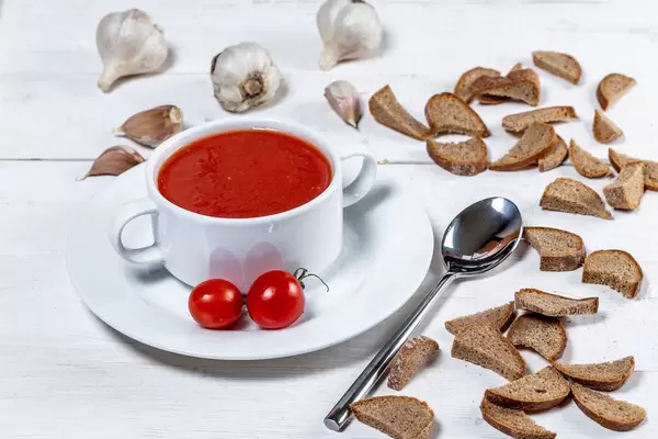 Vegetarian tomato soup with crackers, cherry tomatoes and garlic on white wooden background (Flip 2019)