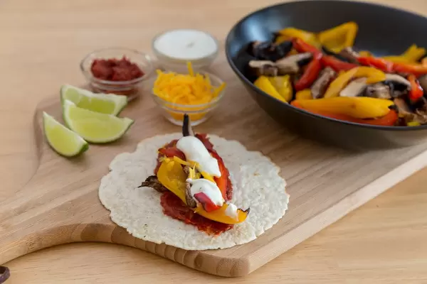 Vegetarische Fajita mit Paprika und Pilzen, gewürzt mit scharfer Tomatensoße und Limettenschmand auf einem Holzbrett mit einer schwarzen Schale auf einem Holzbrett