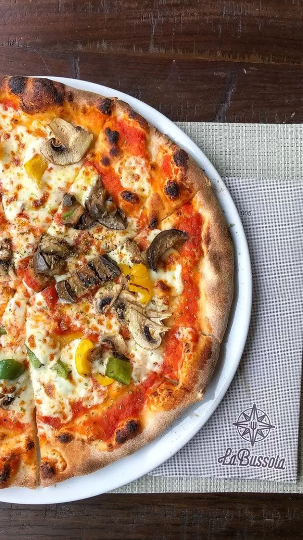 Vegetarische Pizza in der Pizzeria La Bussola, belegt mit Käse, Champignons, gelber und grüner Paprika