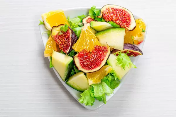 Vegetarischer Salat mit Feigen, Mango, Orange und grünen Salatblättern, auf einem dreieckigen Teller
