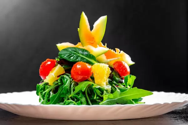 Vegetarischer Salat mit Kräutern, Tomaten und Avocado vor dunklem Hintergrund