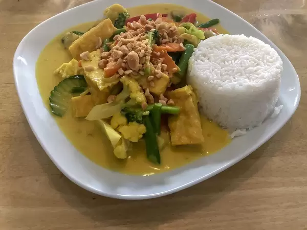 Vegetarisches Mittagessen mit Kurkuma Curry, Gemüse wie Blumenkohl, Paprika, Karotten und weißem Reisturm
