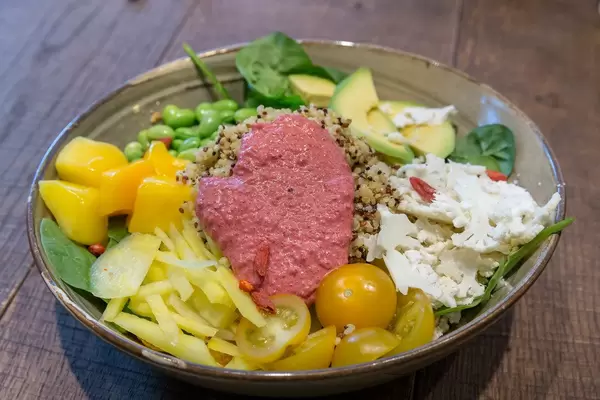 Vegetarisches Mittagessen "Spring Time Bowl" mit Quinoa, Joghurt-Minz-Dressing, Avocado, gelber Bete, Mango, Edamame, Goji, Papadam, Rote-Bete Mayo