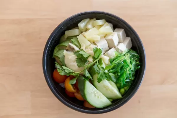 Veggie Bowl Salat mit Gurken, Tomaten, Ananas Tofu und Petersilie in der Aufsicht