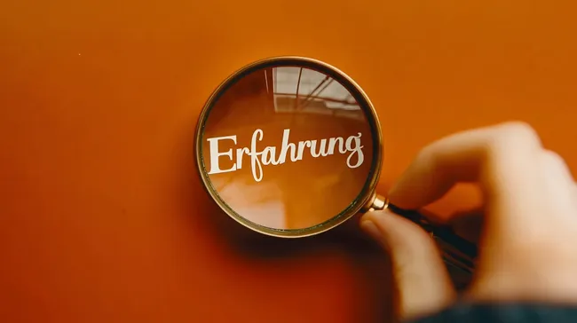 Vergrößerungsglas auf orangefarbenem Hintergrund enthüllt das Wort 'Erfahrung'