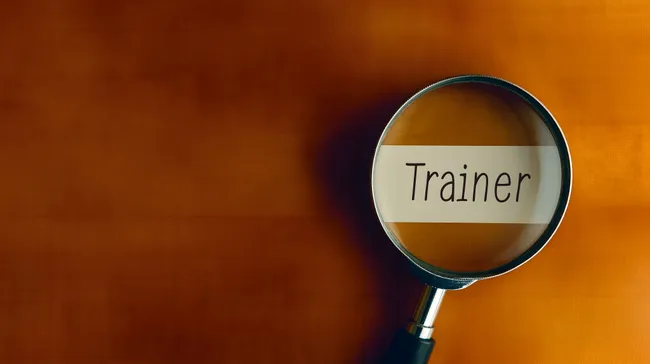 Vergrößerungsglas fokussiert auf Wort 'Trainer'