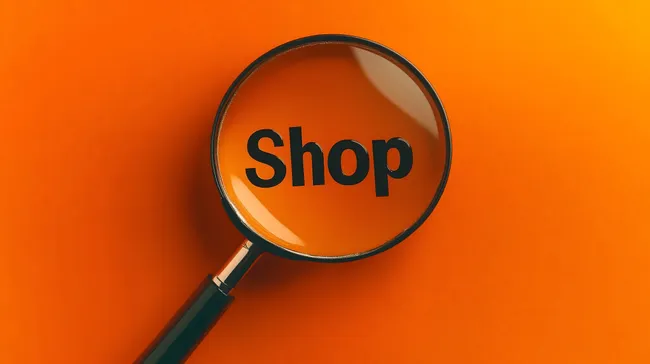 Vergrößerungsglas mit Aufschrift 'Shop' auf orangefarbenem Hintergrund