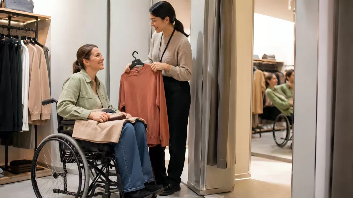 Verkäuferin hilft Frau im Rollstuhl beim Shoppen