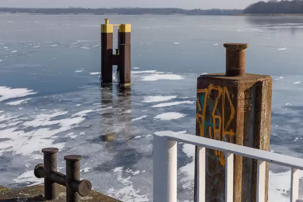 Verrosteter Stahlpfeiler und der zugefrorene Müggelsee im Hintergrund