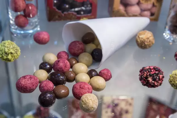 Verschiedene Dragees in bunten Farben fallen aus einer Papiertüte: īsti Lāču gardumi von Laci