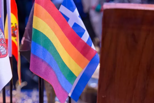 Verschiedene Flaggen von Ländern und eine Flagge in Regenbogenfarben neben Holzschrank