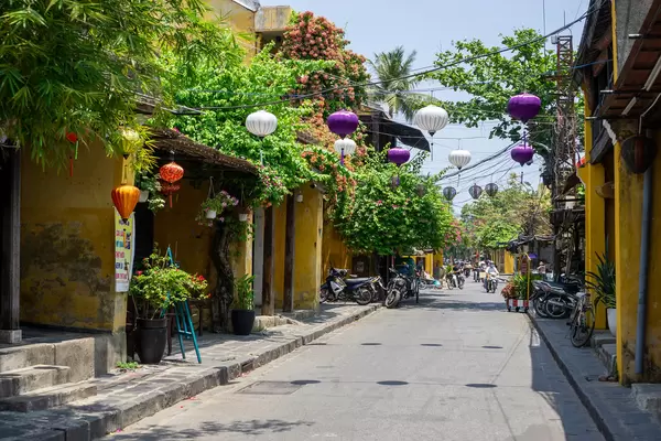 Verschiedene Hängende Lampions, Pflanzen und Bäume neben gelben Gebäuden in der Altstadt von Hoi An, Vietnam
