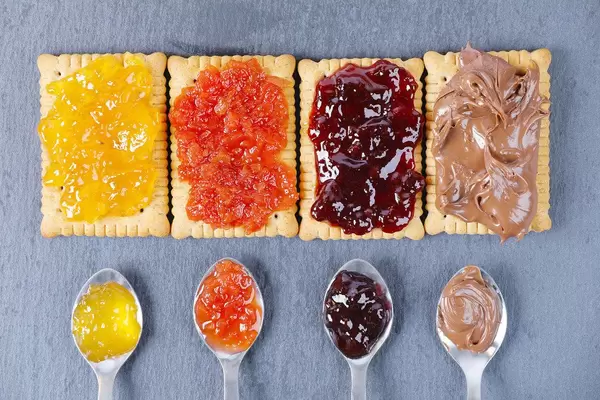 Verschiedene Marmeladen und Aufstriche auf einem Biscuit Keks und kleine Teelöffel daneben