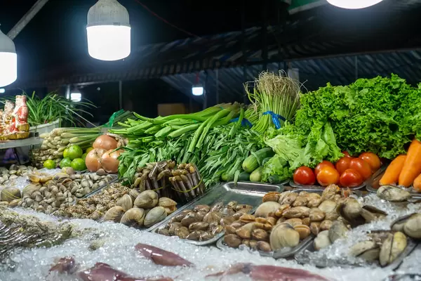 Verschiedene Meeresfrüchte wie Tintenfisch, Garnelen und Muscheln auf Eiswürfeln mit frischem Gemüse im Hintergrund bei einer Straßenküche auf dem Nachtmarkt in Can Tho, Vietnam