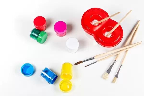 Verschiedene Pinsel, kleine Behälter mit Farben und ein Wasserbehälter auf weißem Hintergrund Draufsicht