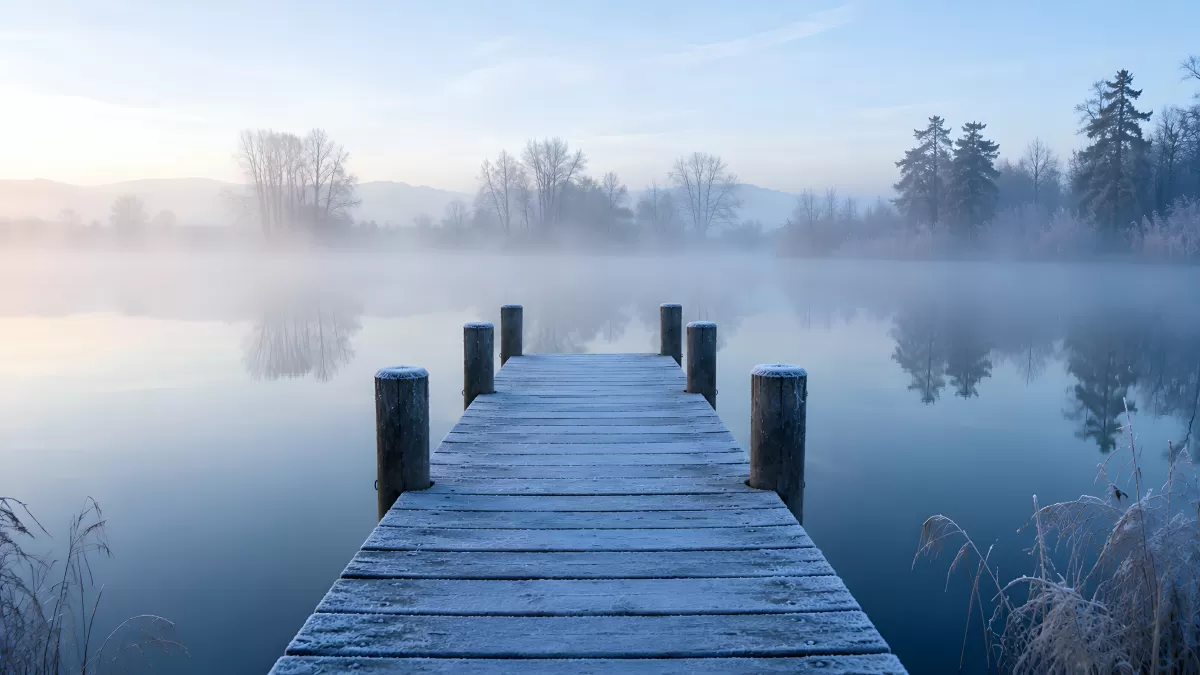 Verschneiter Holzsteg im Morgennebel am See